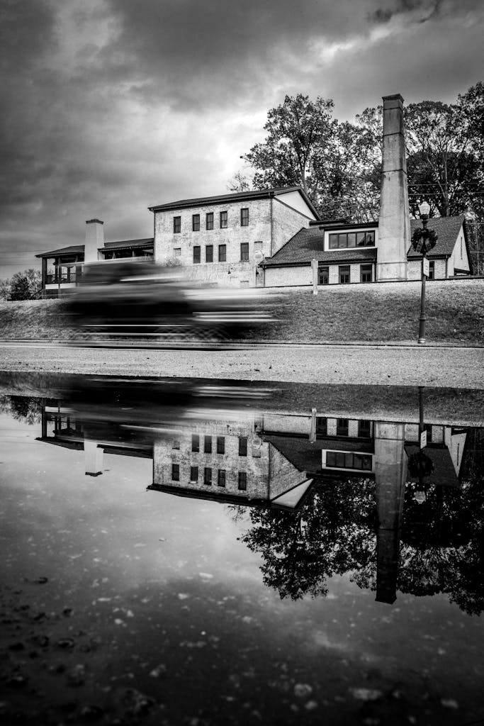 Monochrome image of a building with chimney reflected in water, dramatic mood.